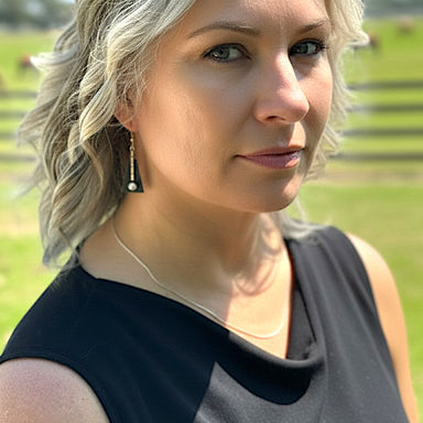 Woman with blonde hair and earrings standing outdoors with a blurred green background