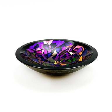 A handcrafted decorative glass bowl with a multicolored dichroic design, showing a mix of purple, black, and colorful pieces creating a visually intricate pattern.