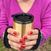 Person holding a wooden travel mug with a black lid outdoors