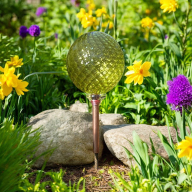 light green garden globe displayed outside in a spring garden surrounded by blooms