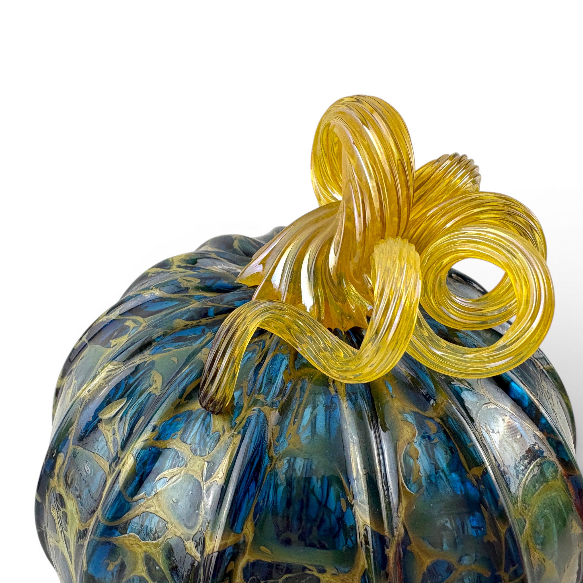 A close-up of a decorative glass pumpkin with a marbled blue and gold pattern and a twisted yellow stem.