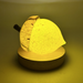 A glowing acorn with a textured yellow body, a dark brown stem, on a round wooden base LED display light, photographed against a warm yellow background.