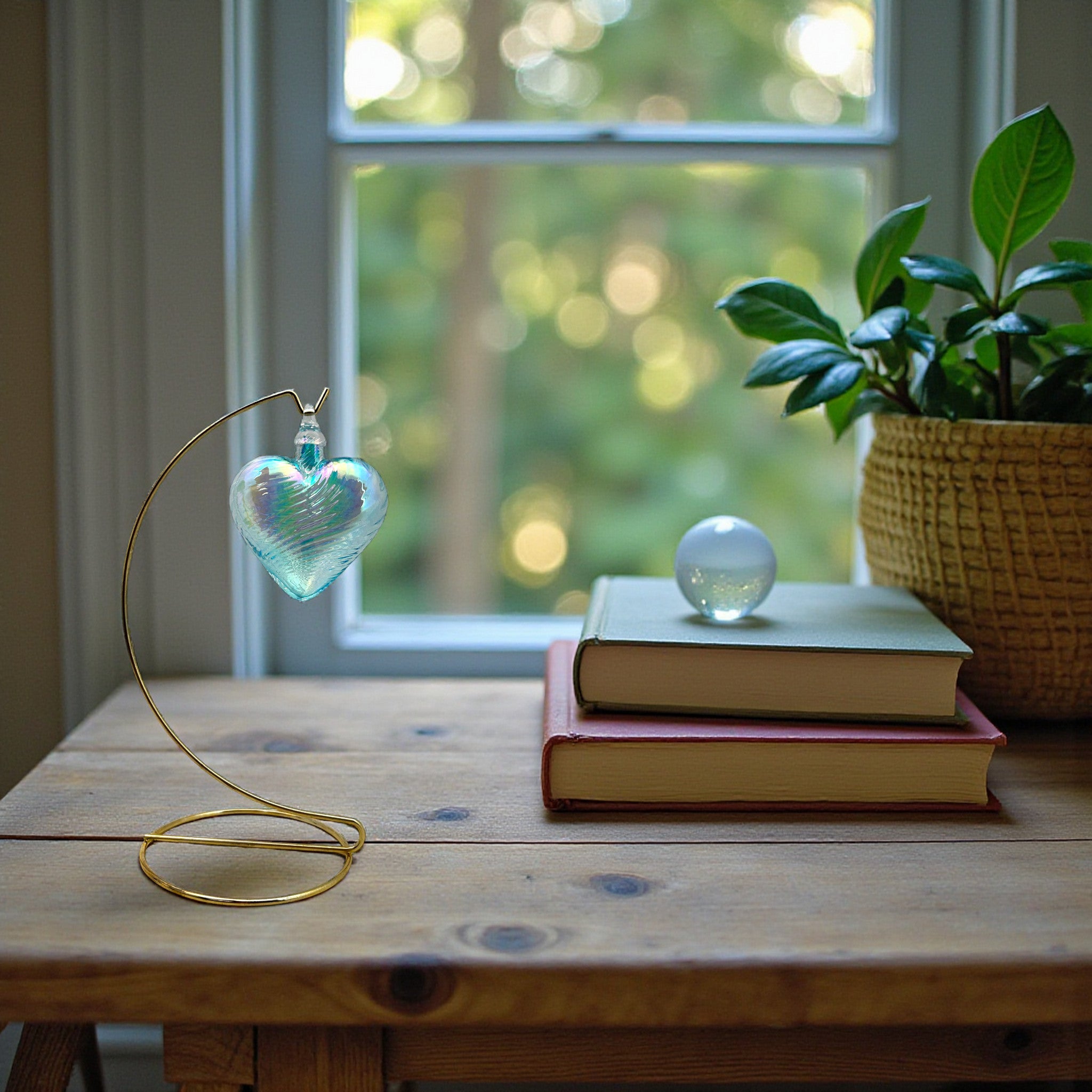 Decorative heart-shaped glass ornament on a wooden table with books and a plant in the background.