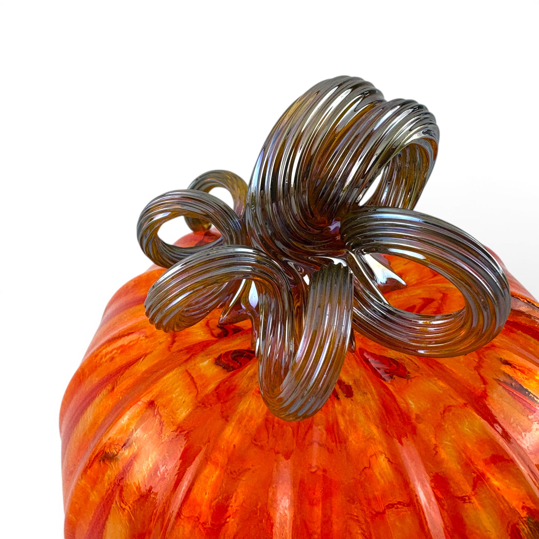 Close-up of an orange and red marbled glass pumpkin with a dark brown coiled stem. 