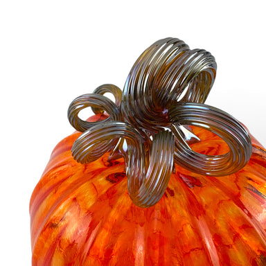 Close-up of an orange and red marbled glass pumpkin with a dark brown coiled stem. 