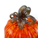 Close-up of an orange and red marbled glass pumpkin with a dark brown coiled stem. 