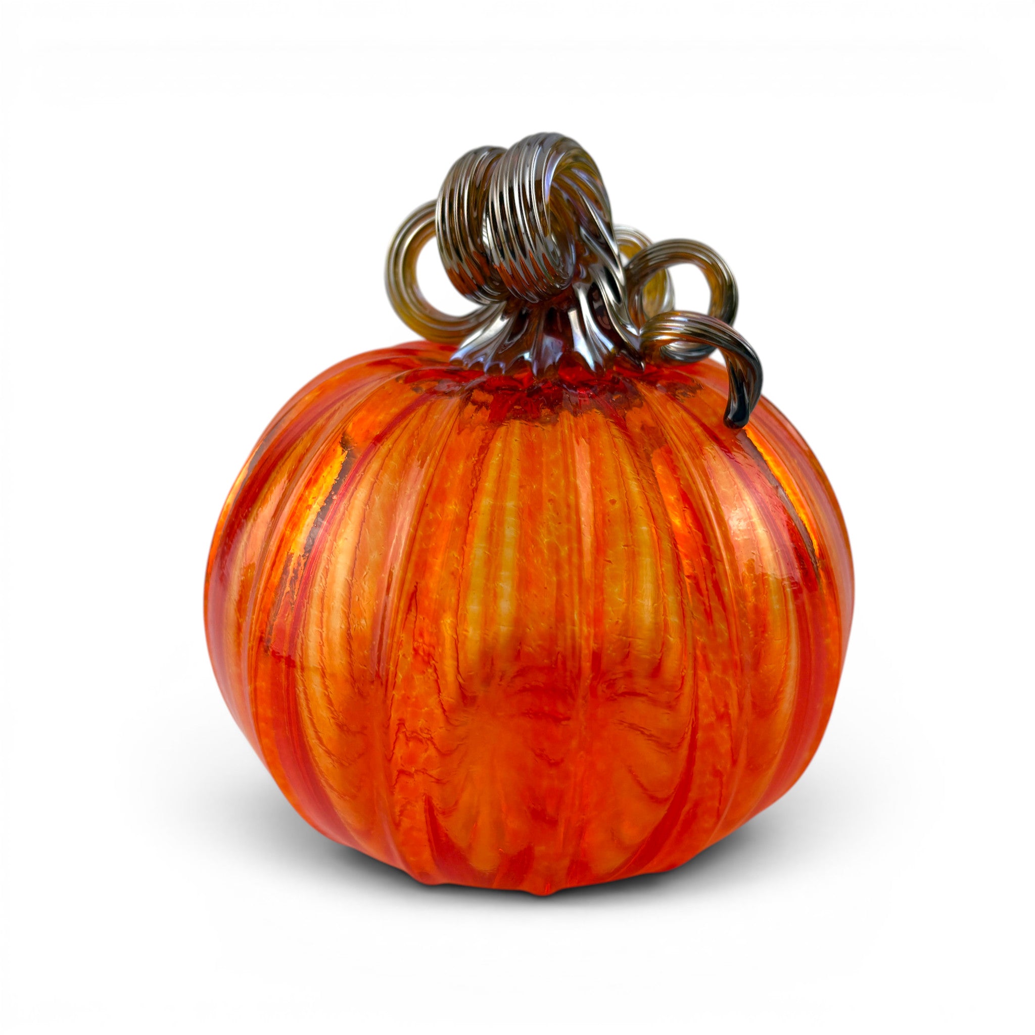 A handcrafted glass pumpkin with a ribbed rounded body, orange and amber marbled coloration, and a dark brown coiled stem. 
