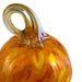 A close-up of a hand-blown glass pumpkin with a curved handle, featuring vibrant orange and yellow marbled patterns on a white background.