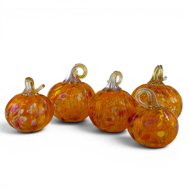 Five decorative glass pumpkins in orange and amber tones with swirling translucent patterns and curled stems, arranged on a white studio background.
