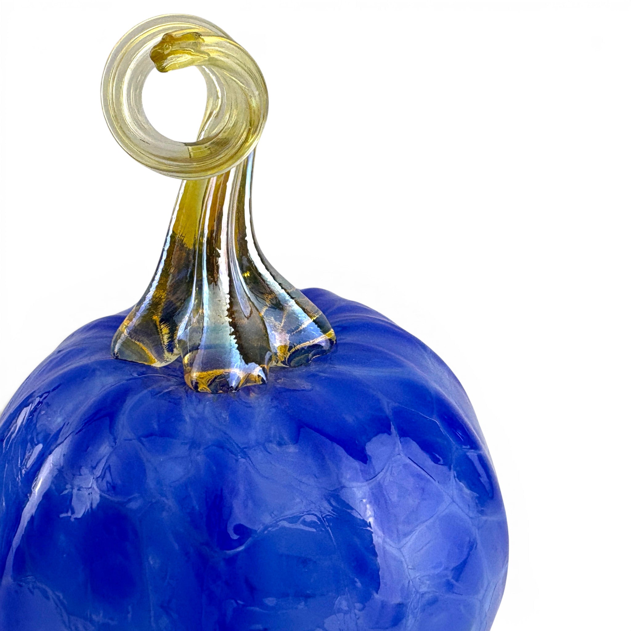 A close-up of a decorative glass pumpkin sculpture with a vibrant cobalt blue body and a twisted amber-yellow stem on a white background.