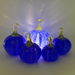 Five decorative glass pumpkins in cobalt blue and clear glass, with one larger central pumpkin glowing from within and four smaller pumpkins arranged around it on a light background.