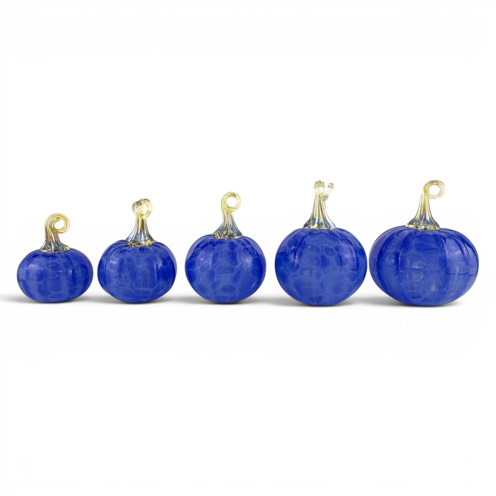Five small cobalt blue glass pumpkins with gold-toned stems and loops, arranged in ascending size order on a white background.