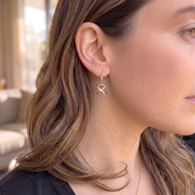 A close-up side profile of a woman wearing a delicate silver dangle earring shaped like a stylized secret heart. 