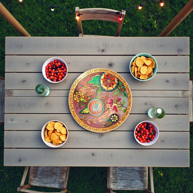 Wooden table with decorative lazy susan tray and snacks on a grassy background outdoors in the spring