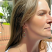 A close-up side profile of a woman wearing a delicate hoop earring with a textured lower half, set against an outdoor patio background.
