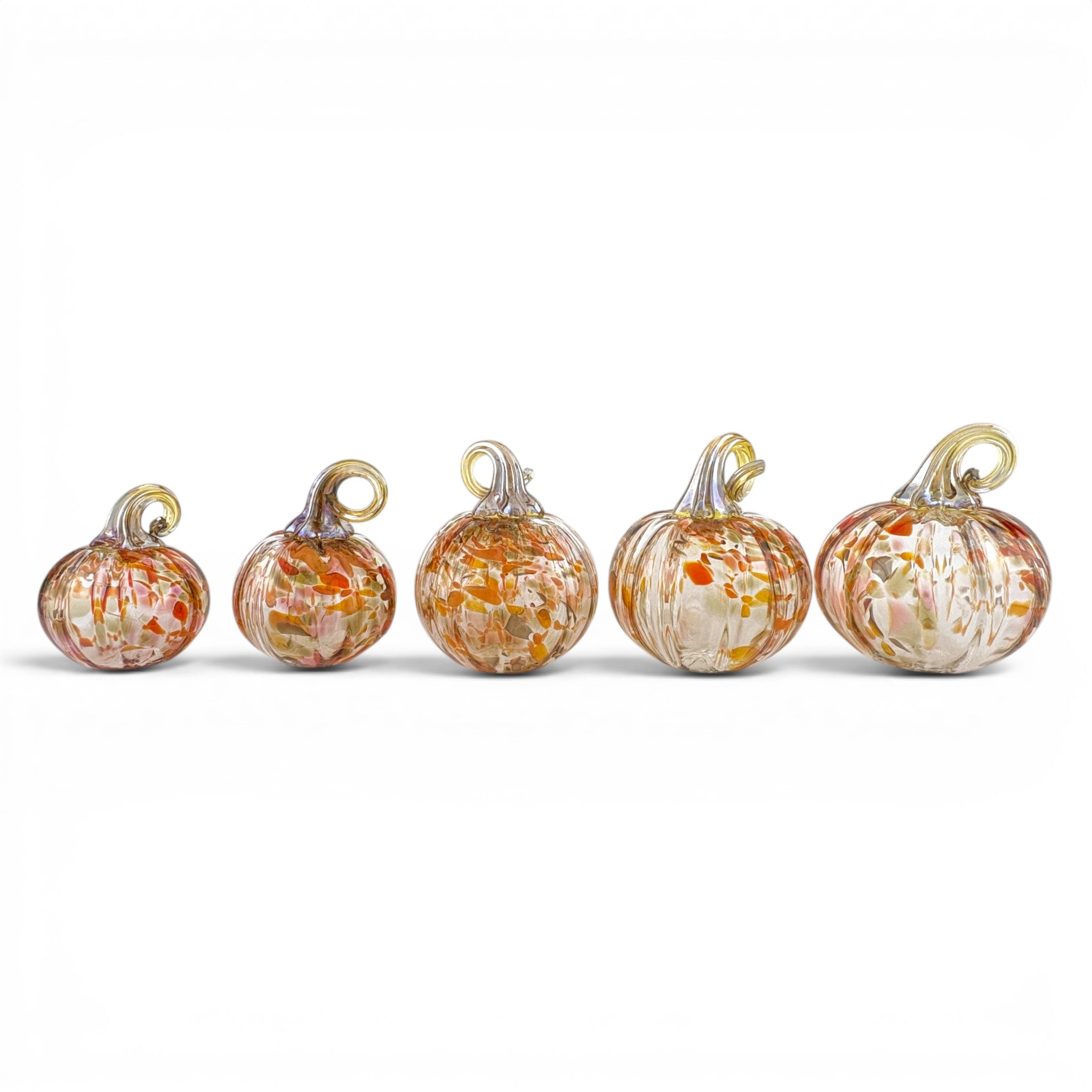 Five small glass pumpkins arranged in a row on a white background, each with a loop at the top for hanging. The pumpkins are made of clear glass with orange, red, and white marbled patterns and have metallic gold and silver stems.