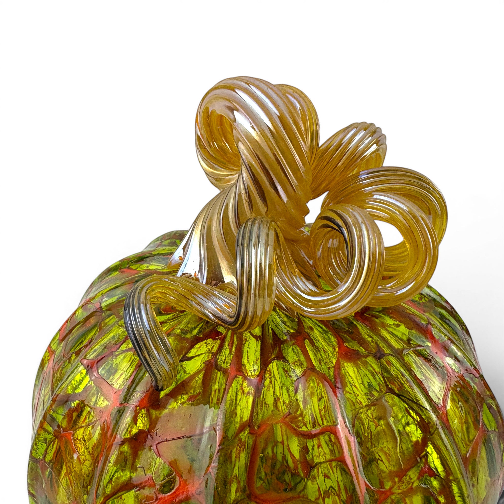A close-up of a hand-blown glass pumpkin with a twisted stem, featuring a vibrant green body with red and yellow marbling and a golden-yellow stem.
