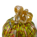 A close-up of a hand-blown glass pumpkin with a twisted stem, featuring a vibrant green body with red and yellow marbling and a golden-yellow stem.
