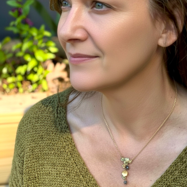 Woman wearing a gold necklace with a green leaf pendant outdoors