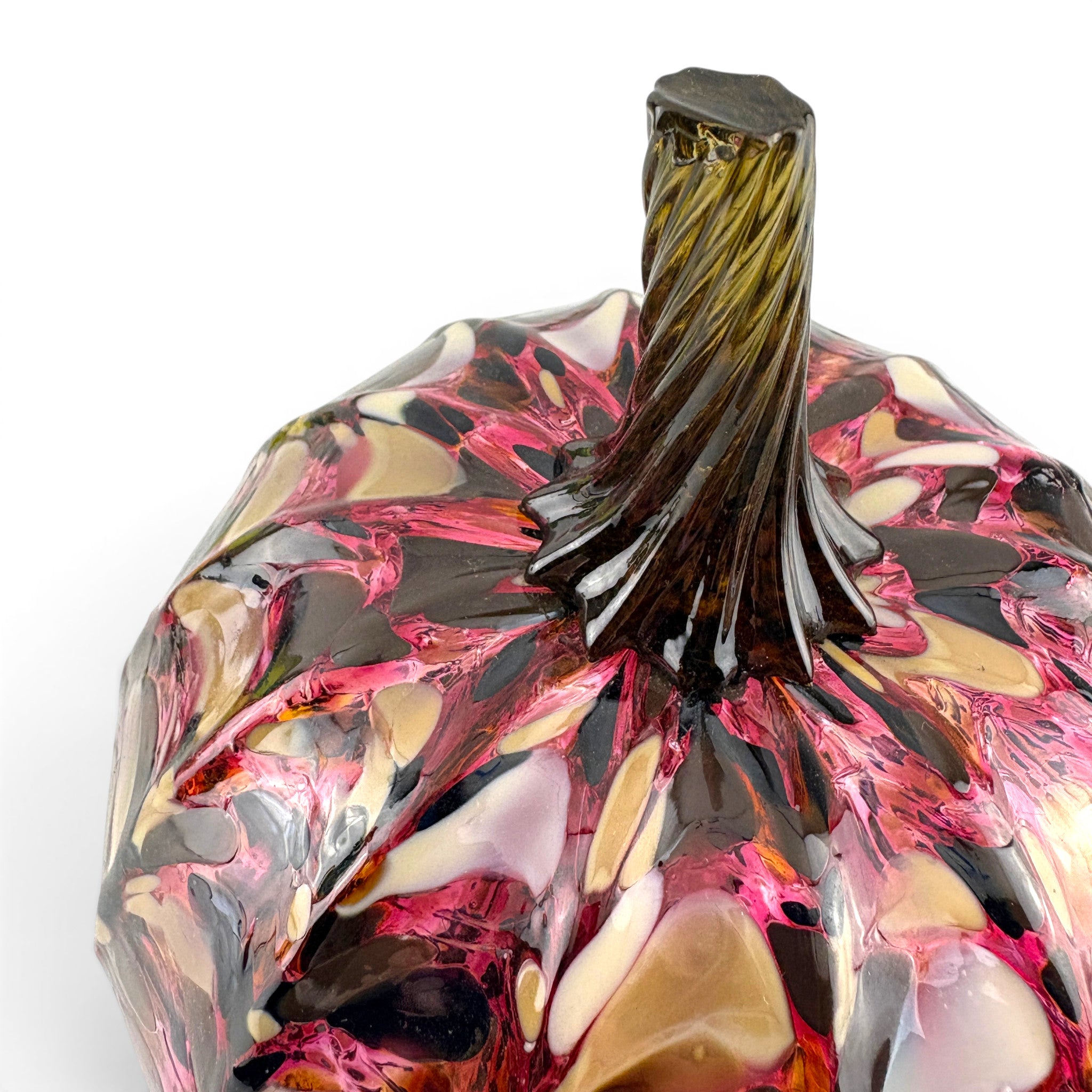 A close-up of a handcrafted glass pumpkin with a glossy, marbled pattern of pink, amber, brown, and black, featuring a textured dark stem. 