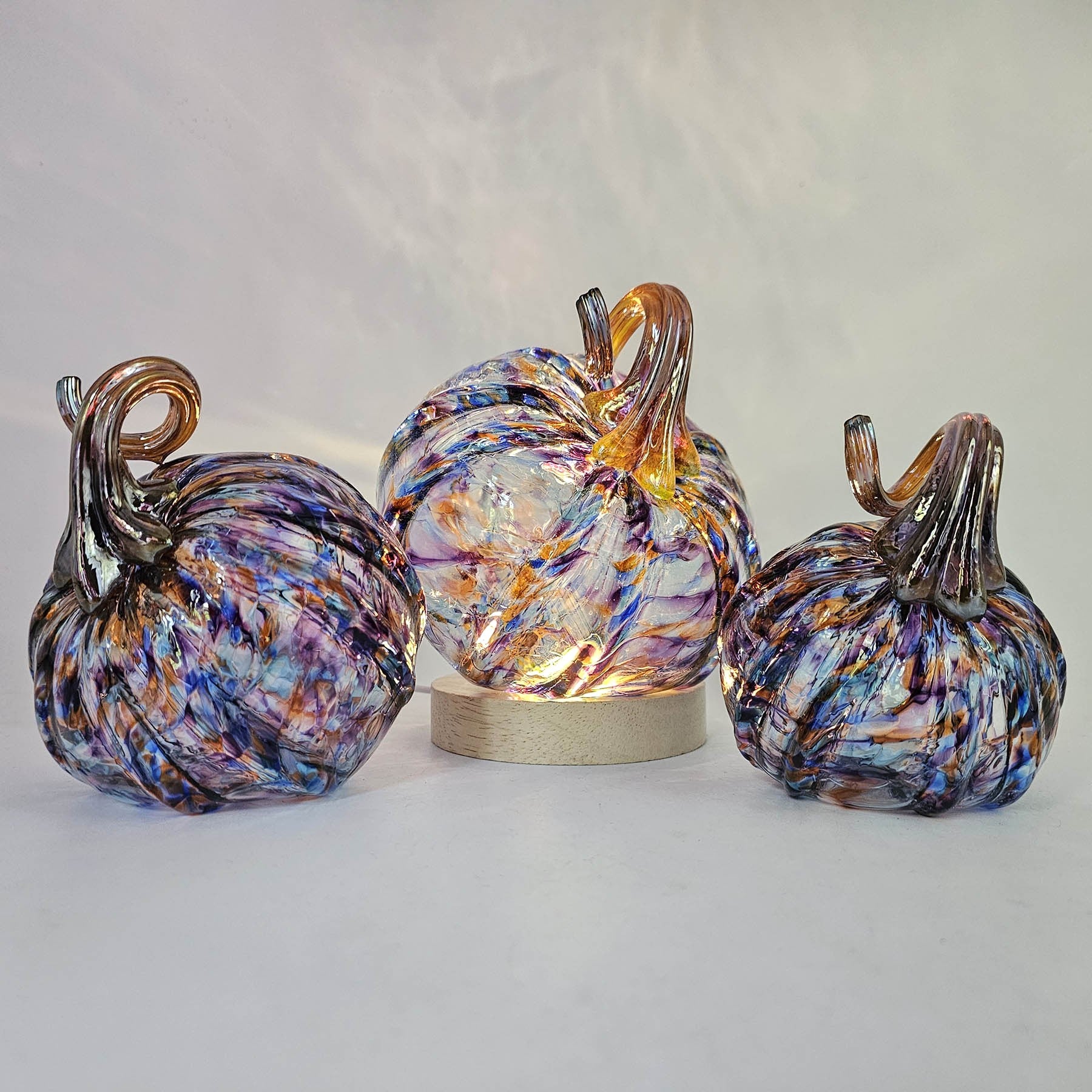 Three multicolored glass pumpkins on a light gray background