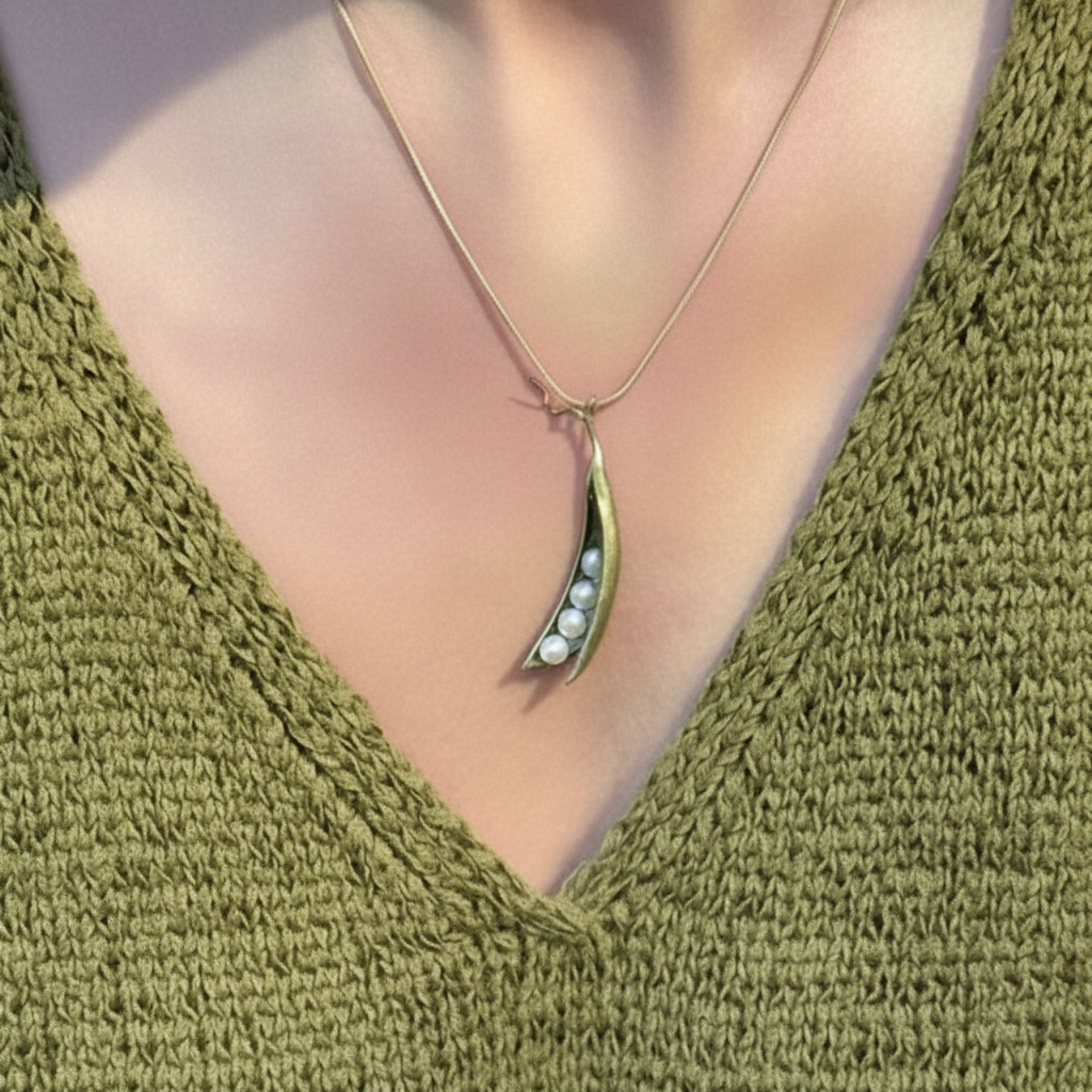 A close-up of a person wearing a delicate gold necklace with a crescent-shaped pendant that holds small white pearls, styled with an olive green knit V-neck top.