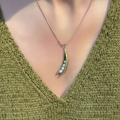 A close-up of a person wearing a delicate gold necklace with a crescent-shaped pendant that holds small white pearls, styled with an olive green knit V-neck top.