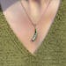 A close-up of a person wearing a delicate gold necklace with a crescent-shaped pendant that holds small white pearls, styled with an olive green knit V-neck top.