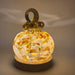 A handcrafted glass pumpkin with a warm white glow, featuring embedded yellow and orange leaf patterns, a dark brown glass stem loop, sitting on an LED display light with a round wooden base.