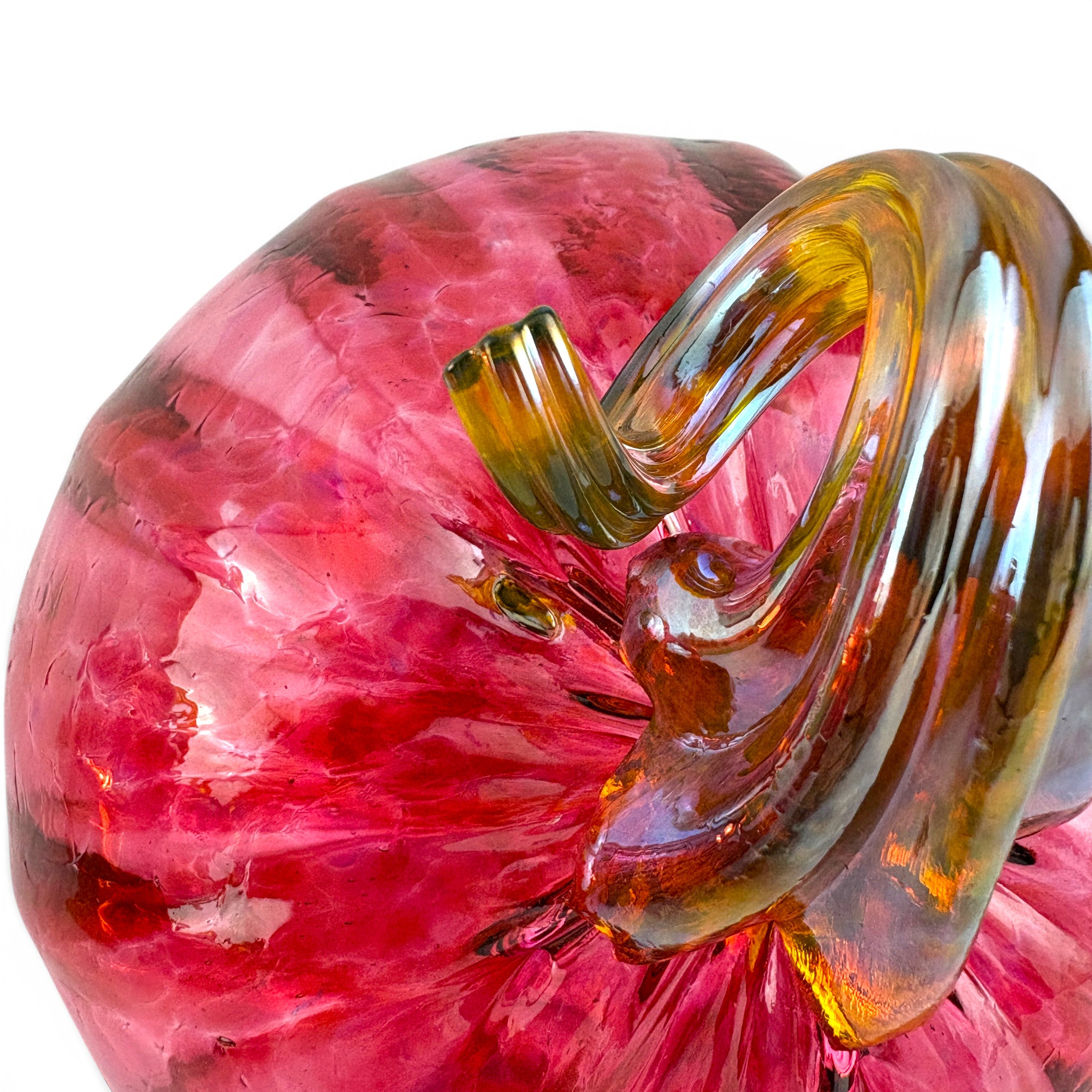 A close-up of a hand-blown glass sculpture, featuring a textured, translucent pink body with a glossy, curled amber-brown glass stem against a white background.