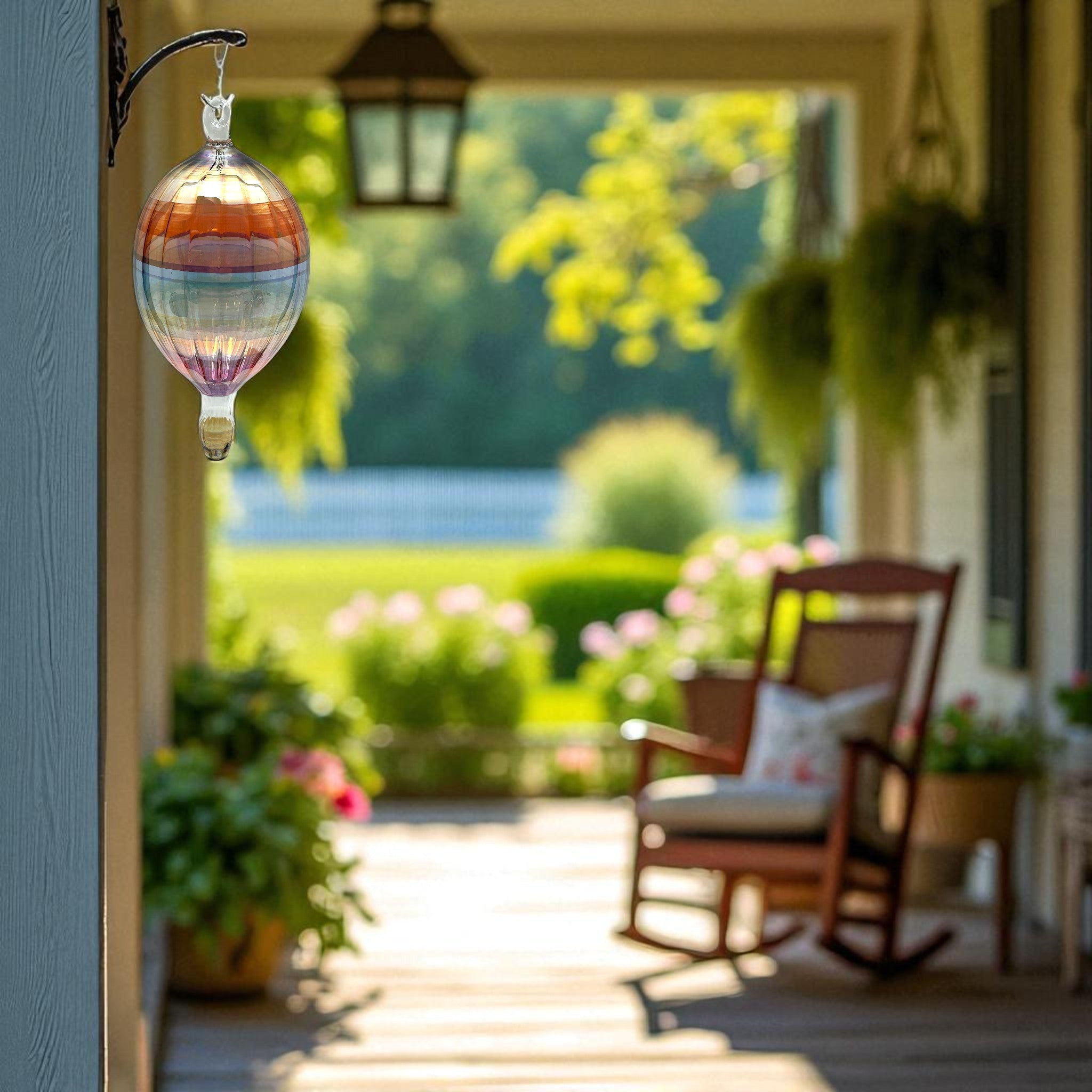 Decorative glass hanging hot air balloon decorative ornament on a porch with a view of a garden and lake.