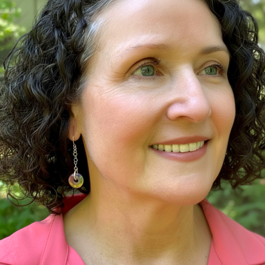 Woman with curly hair wearing earrings, smiling outdoors