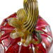 A close-up of a hand-blown glass pumpkin with a textured red body and a ribbed amber-yellow stem featuring dark brown stripes.  