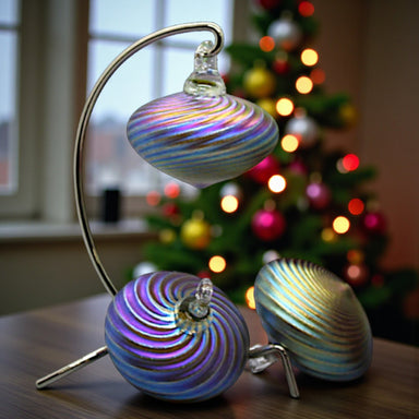 Decorative glass ornaments on a stand with a Christmas tree in the background
