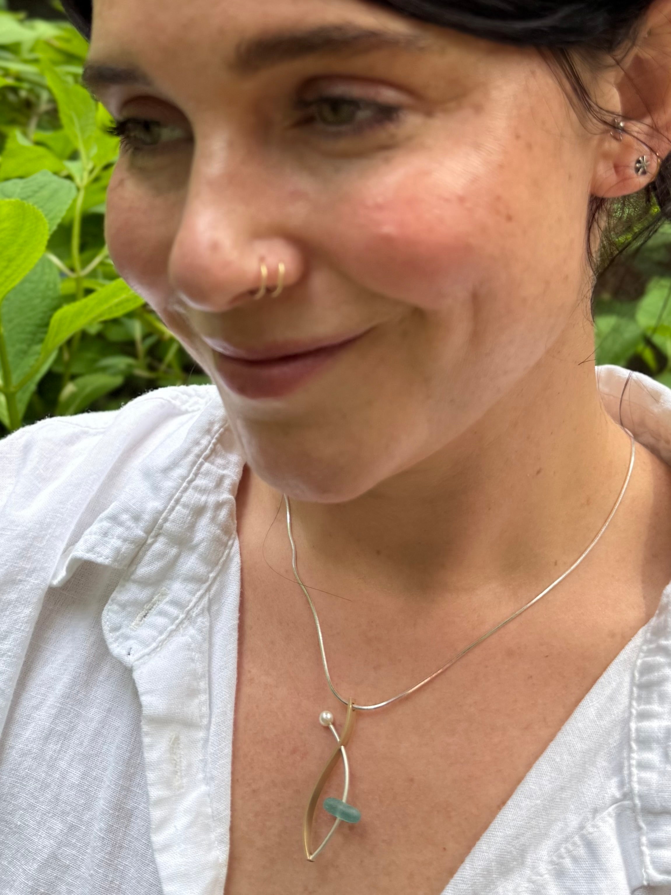 Woman wearing a gold necklace with a green stone against a natural background