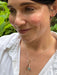 Woman wearing a gold necklace with a green stone against a natural background
