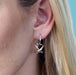 Close-up of a person wearing a silver secret heart earring against a light blue background.
