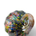 A close-up of a faceted glass container with a curved handle, featuring an iridescent finish that reflects multiple colors including green, blue, yellow, pink, and purple. 