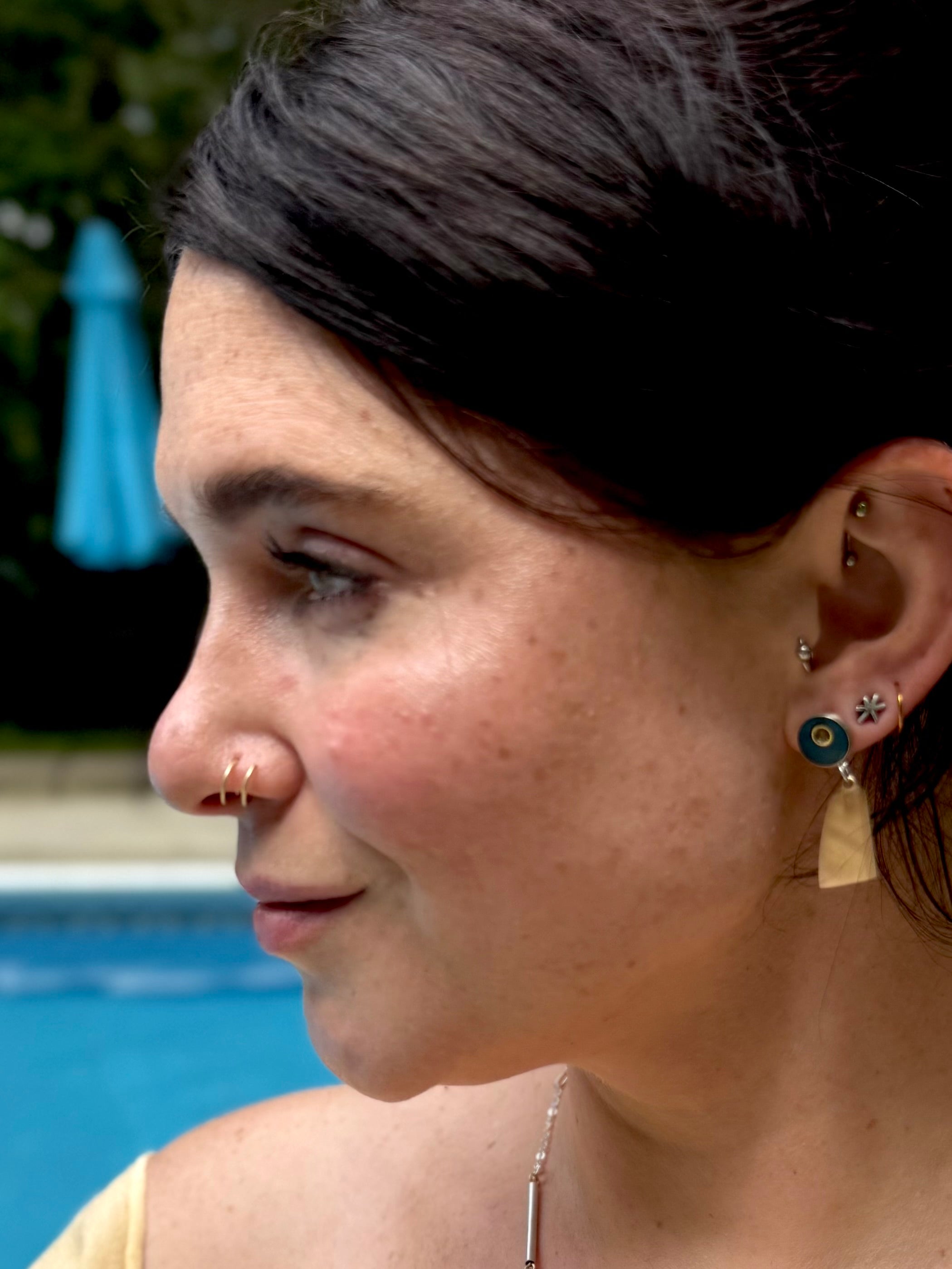 Close-up of a woman's face with earrings, outdoors near a pool.