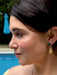 Close-up of a woman's face with earrings, outdoors near a pool.