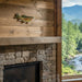 Wooden wall with a fish sculpture above a stone fireplace, with a scenic view of trees and mountains through a window.