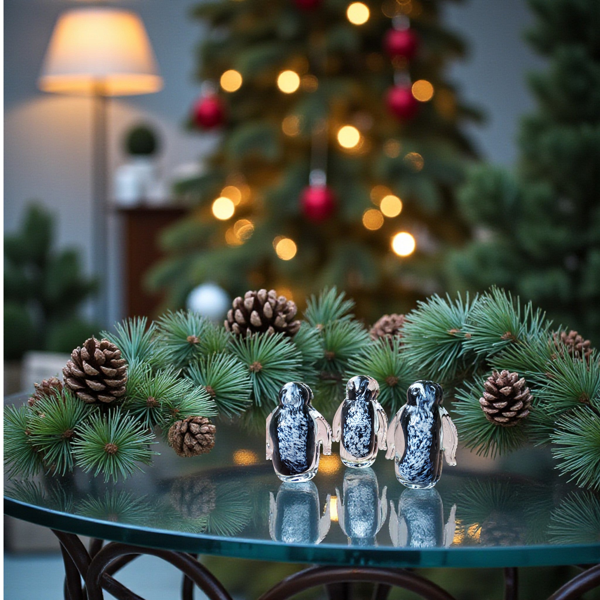 Decorative penguins and pinecones on a glass table with a Christmas tree in the background.