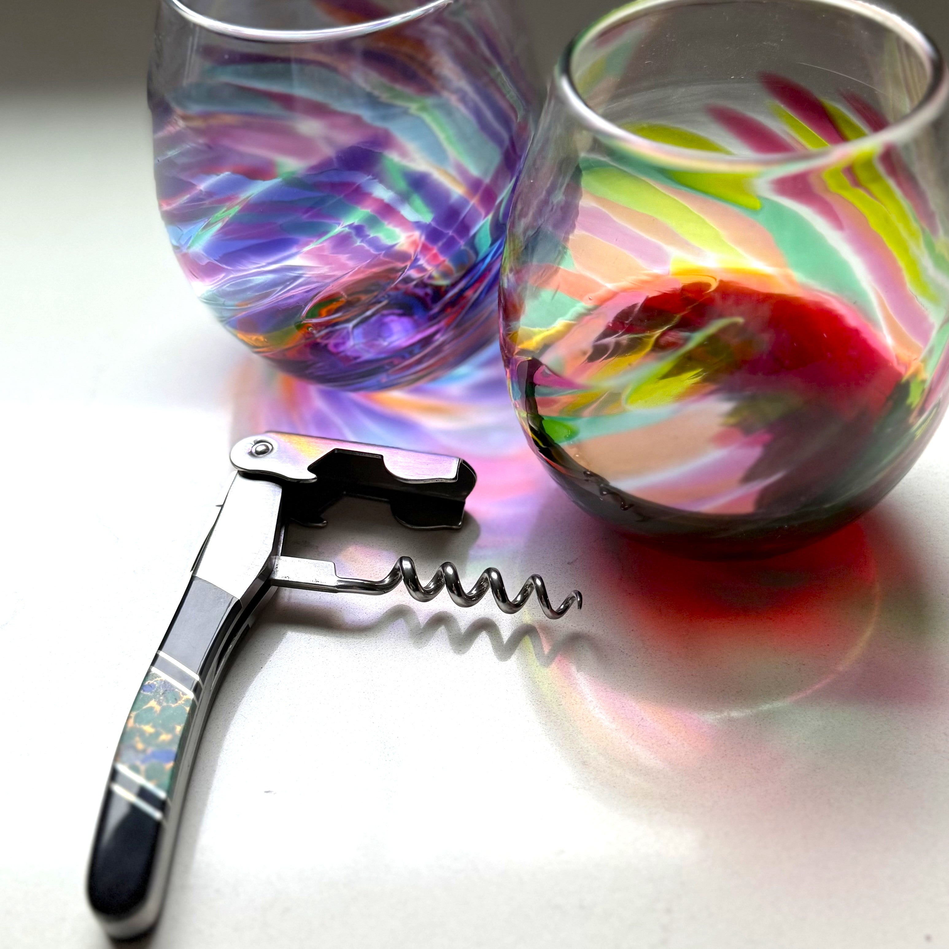 Two colorful wine glasses with a corkscrew on a white surface