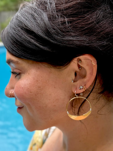Close-up of a person wearing gold hoop earrings with a blurred background