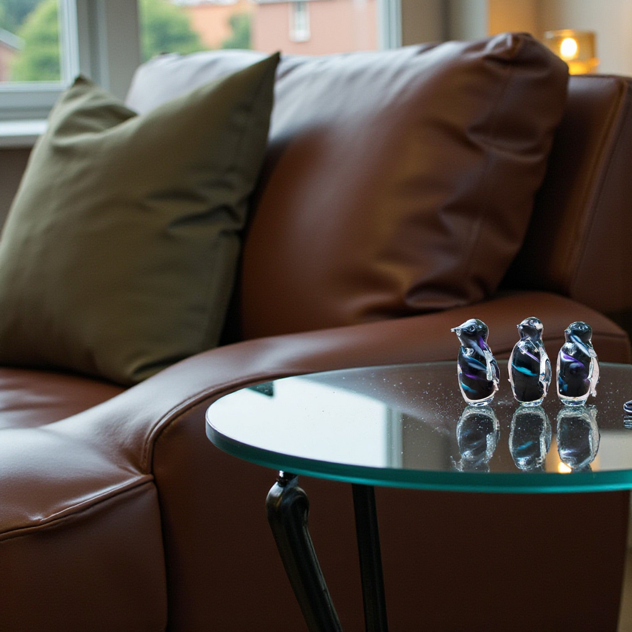 Glass table with decorative items in front of a brown leather sofa.