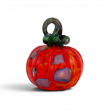 A handcrafted glass pumpkin with a vibrant red and orange marbled body, purple and blue inclusions, and a dark green to black twisted stem.