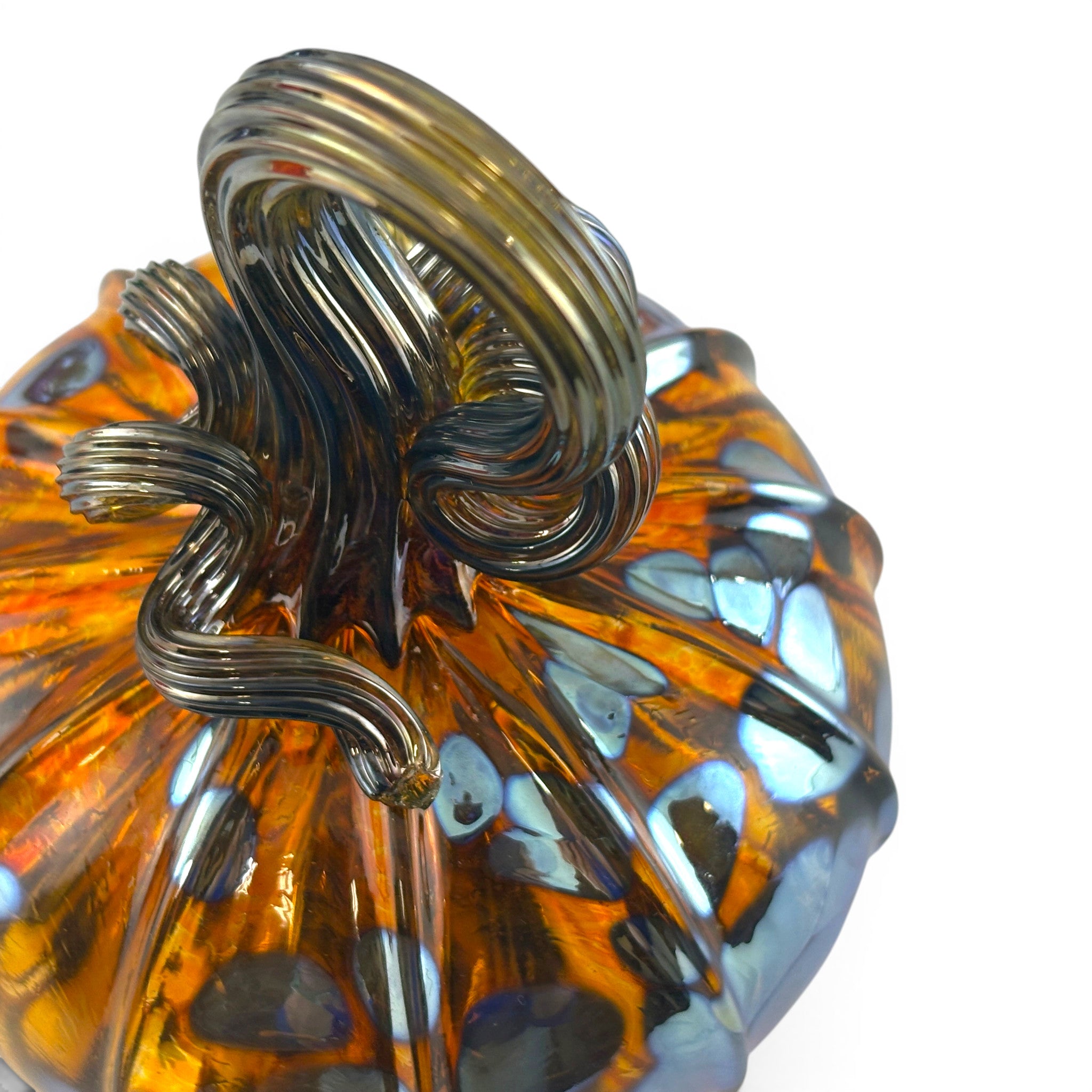 A close-up of a handcrafted glass pumpkin with a ribbed amber-orange body, dark gray smoky glass detailing, and a matching dark gray stem. 
