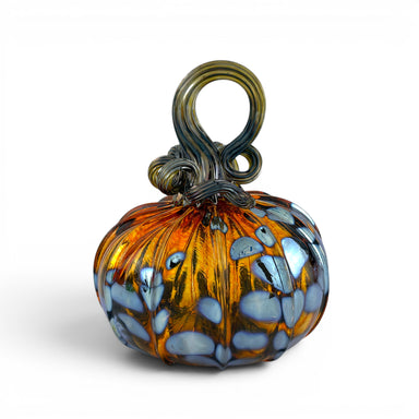 A hand-crafted glass pumpkin with a swirling amber orange body, light blue petal-like patterns, and a dark green to black looped stem. 