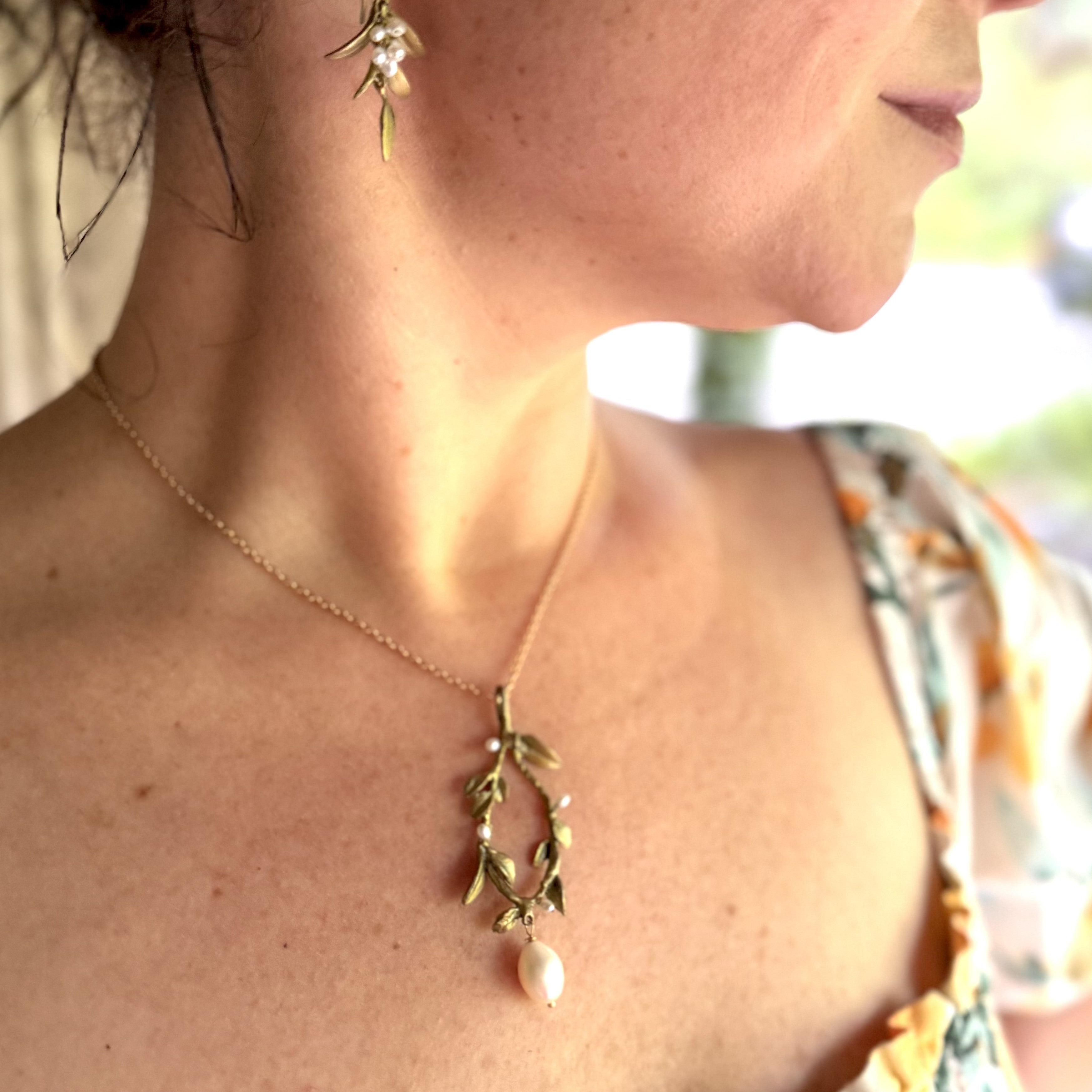 Close-up of a person wearing a gold necklace with a leaf design and pearl pendant.