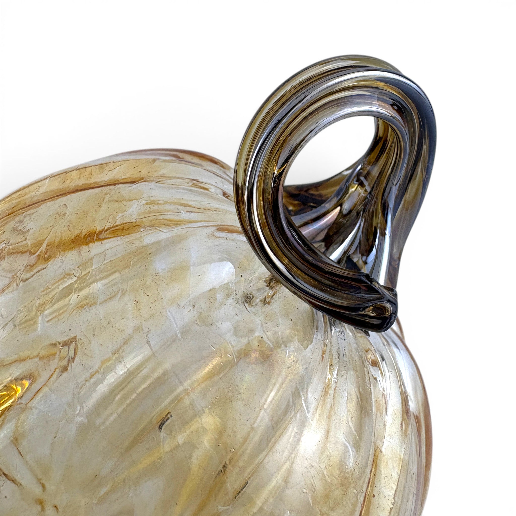 A close-up of a decorative glass pumpkin with a ribbed body in milky amber and clear glass, featuring a thick, twisted dark smoky-brown handle. 